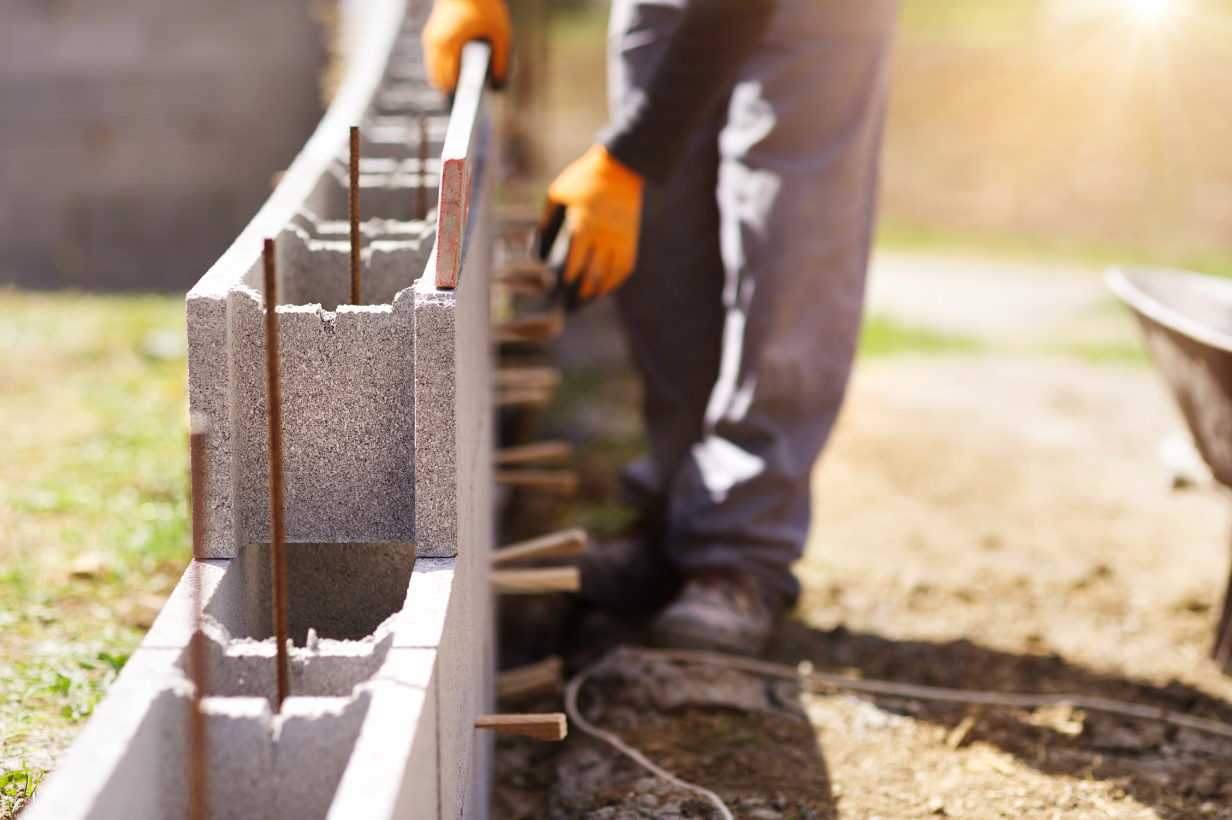 Mason aligning a concrete block wall with a level, with vertical reinforcement visible